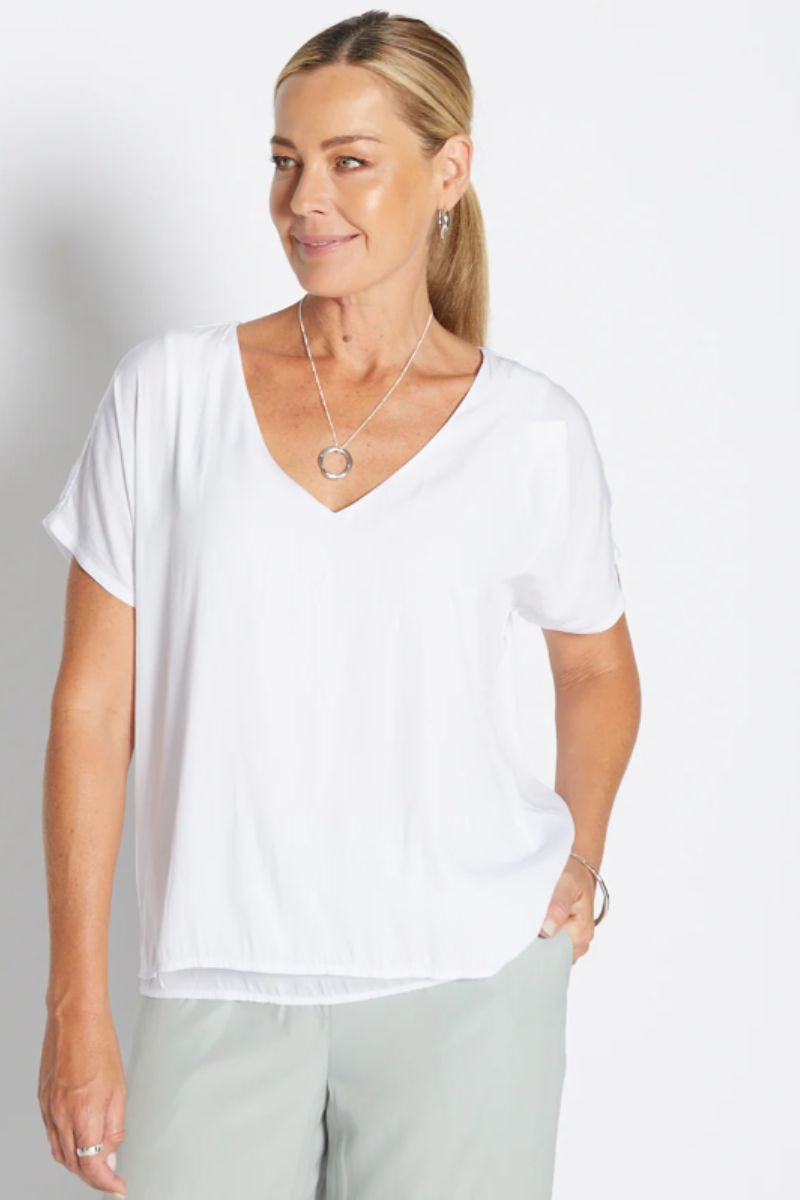 Woman wearing a white V-neck t-shirt and light gray pants against a plain background