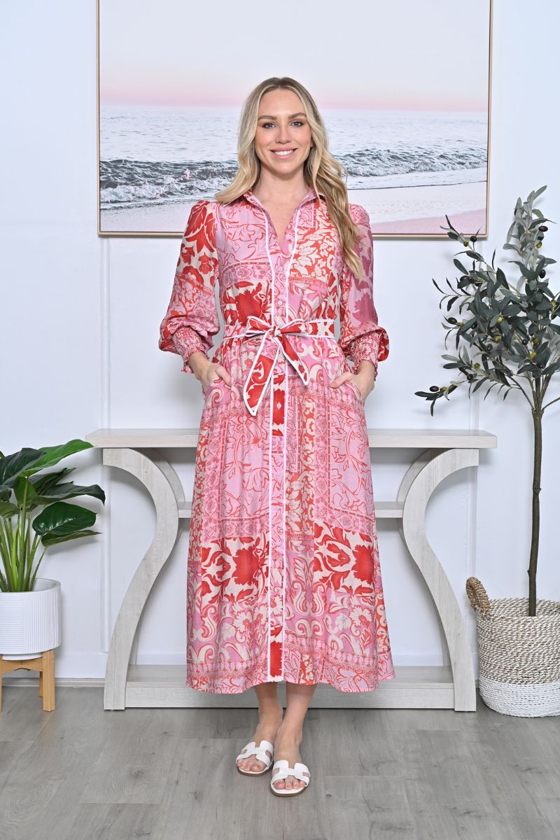 Woman wearing a red patterned dress standing in a room with a decorative table and plants.
