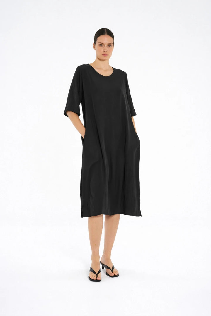 Woman wearing Plaza Dress in Black by Mela Purdie F67 3004, three-quarter view with low-heeled black sandals.